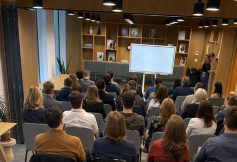 Tým na firemním workshopu sleduje prezentaci v moderní zasedací místnosti.